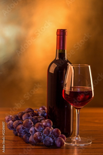 Red wine bottle with glass and grape on gold background