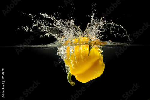 Yellow bell pepper falling in water with splash on black background