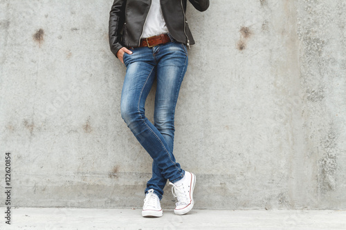 Shapely female legs in sneakers and jeans near a concrete wall photo