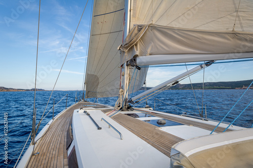 Sailing boat teak deck and hoisted sails, view from the cockpit to the bow.