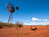 an old rusty wind turbine and cattle feeder,  in the harsh arid red landscape of the australian outback bush.