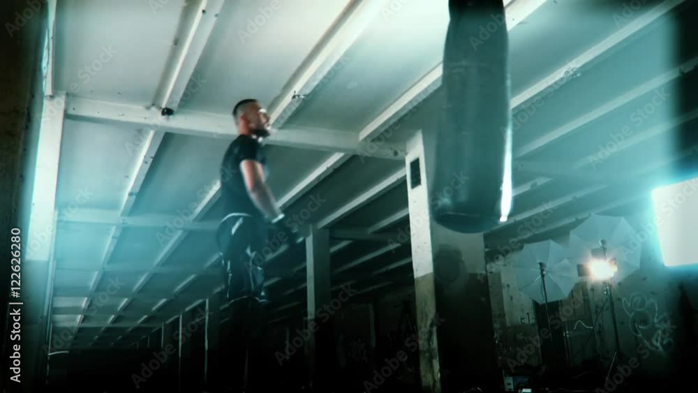 Male Athlete boxer punching bag with dramatic edgy lighting in a dark studio Male Athlete boxer punching bag with dramatic edgy lighting in a dark studio