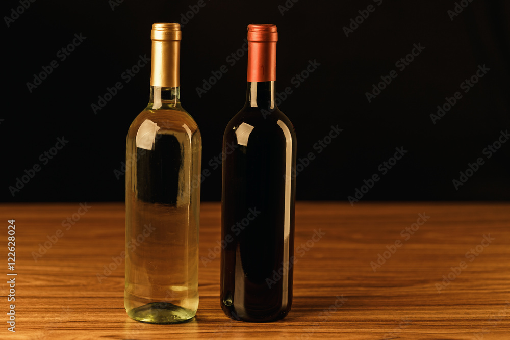 Red and white wine bottles on wooden table and black background