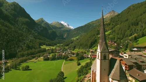 Aerial footage of St Vincent church in Heiligenblut in austrian Alps, popular tourist destination with highest peaks of Austria in the background.