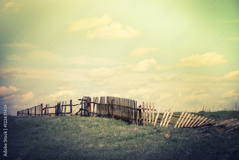 Sunny day in countryside. Summer landscape with old broken fence at pasture  under blue cloudy sky. Nature background in vintage style