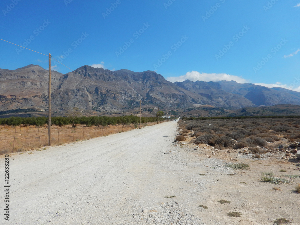 A dirty road in a flat landscape with mountains in background