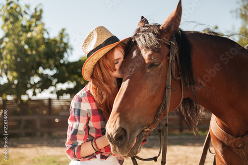 Beautiful woman cowgirl standing and kissing her horse