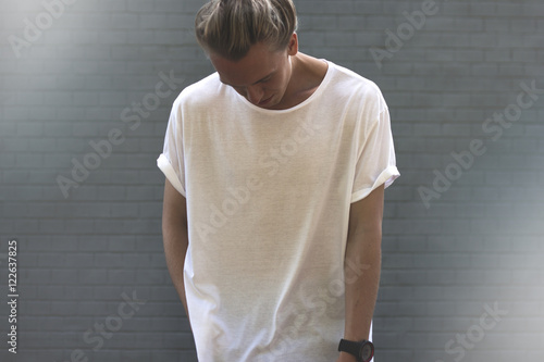 Guy with blond hair in a blank white t-shirt stands with his hea