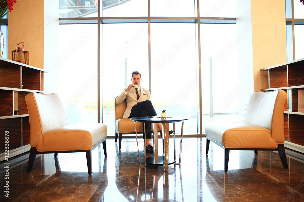 Portrait of handsome successful man drink coffee sitting in coffee shop, business man having breakfast at hotel lobby.