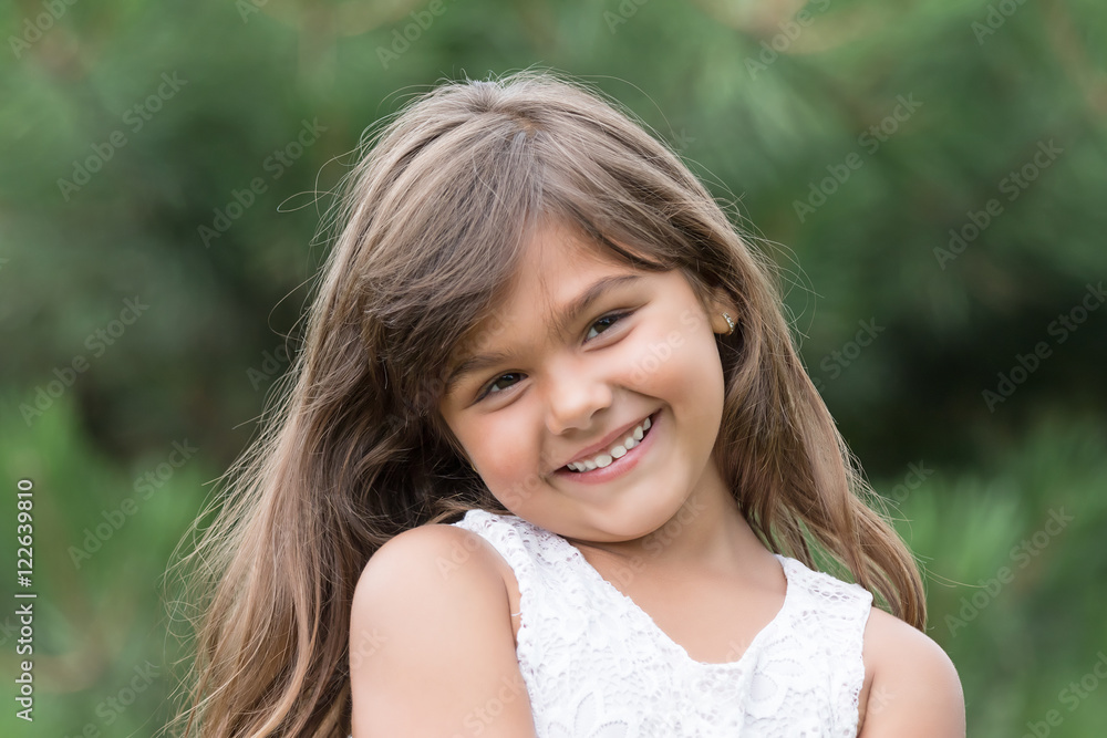 Fototapeta premium Portrait of smiling tanned brunette little girl outdoors. Little girl is looking at the camera