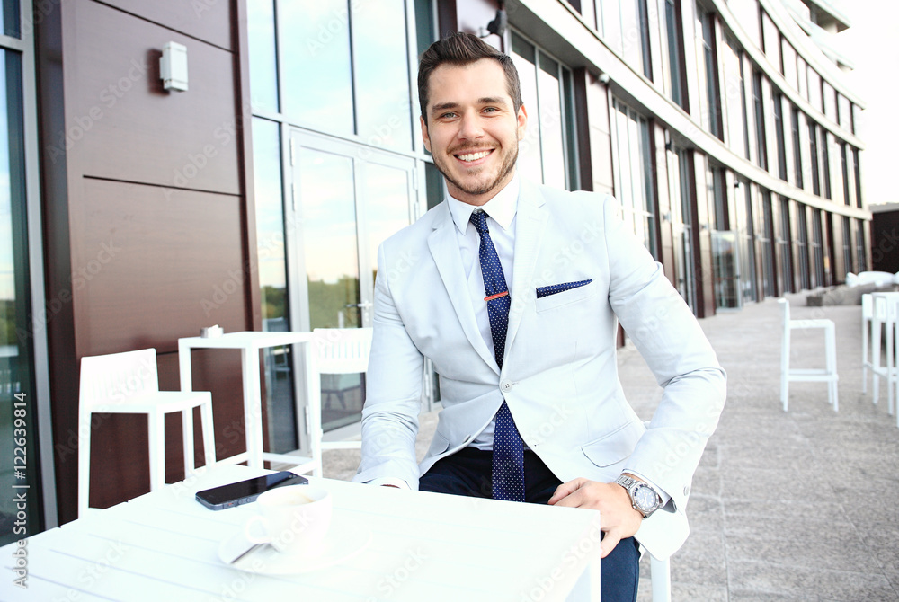 Fototapeta premium Portrait of handsome successful man drink coffee, business man having breakfast sitting on beautiful terrace