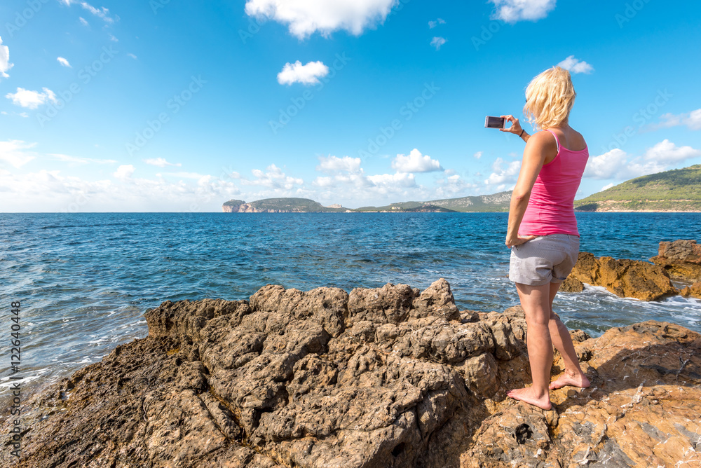 Young beautiful woman taking picture of coast Capo Caccia bay, Sardegna, Italy, Mediterranean Sea, sunny day, summer season