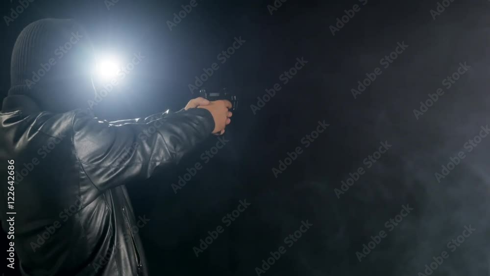 masked criminal holding gun into a dark room back lit masked criminal holding gun into a dark room back lit