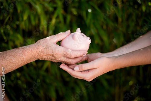 close up of elderly woman hand giving piggy bank money legacy to young person
