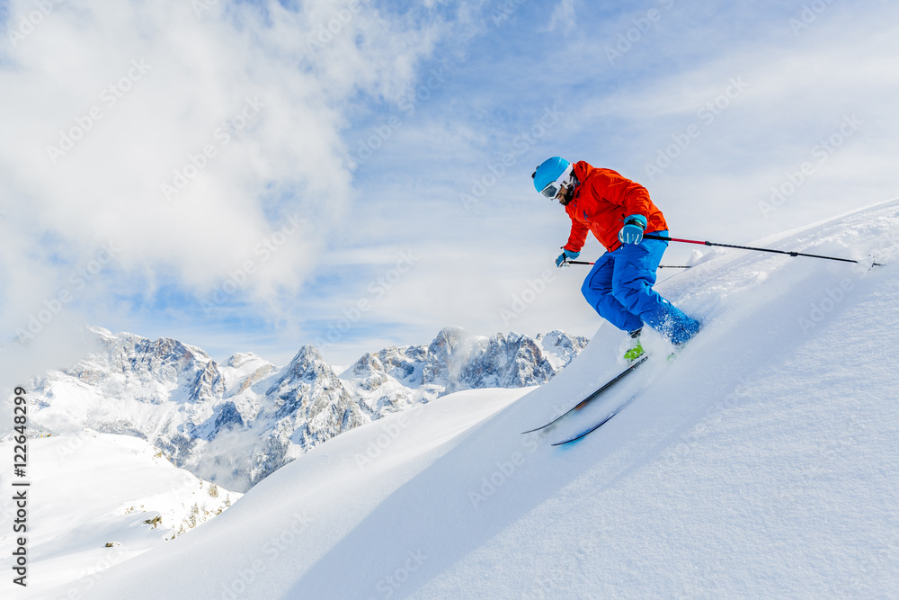 Skier skiing downhill in high mountains in fresh powder snow.