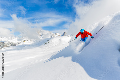 Skier skiing downhill in high mountains in fresh powder snow. 