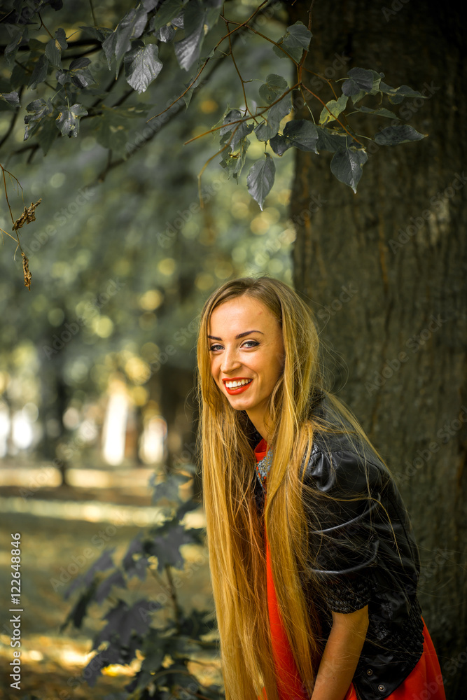 Beautiful girl with long hair in red dress and leather jacket sitting on the grass