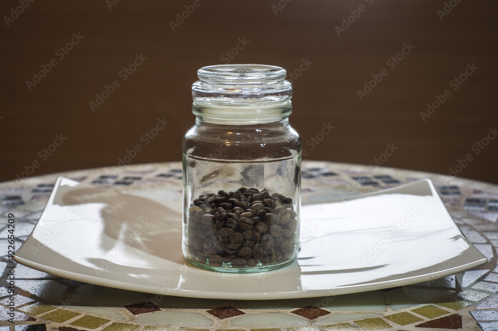 Obraz premium ziarnista kawa w szklanym słoiku na białym talerzyku, coffee beans in a glass jar