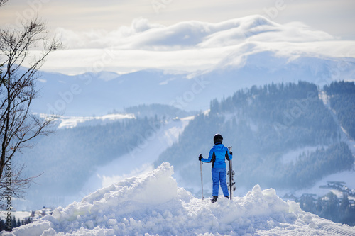 Rear view of woman skier standing on top of the mountain and enjoying the view on beautiful winter mountains on a sunny day. Winter sports concept. Carpathian Mountains