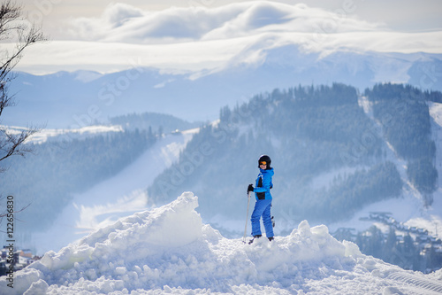 Rear view of skier standing on top of the mountain, looking to the camera and enjoying the view on beautiful winter mountains on a sunny day. Winter sports concept.