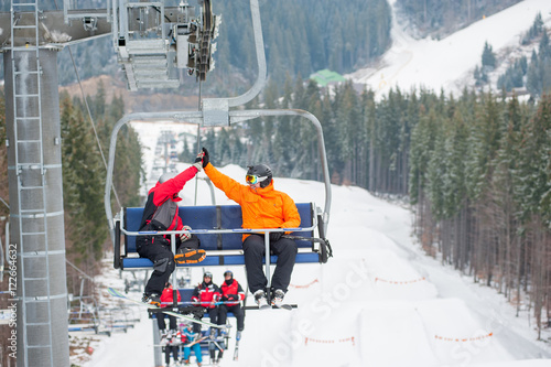Two male ride the ski chair lift up the mountain together and giving each other a high five, having a fun time. Carpathian mountains, Ukraine