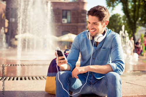 Handsome smiling man with headphones listening music near founta photo