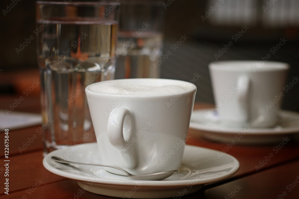White cup of coffee and glasses of water on the wooden table