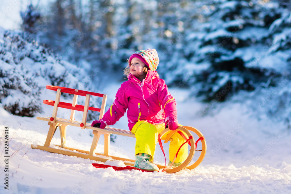Little girl having fun on a sledge in snowy winter forest