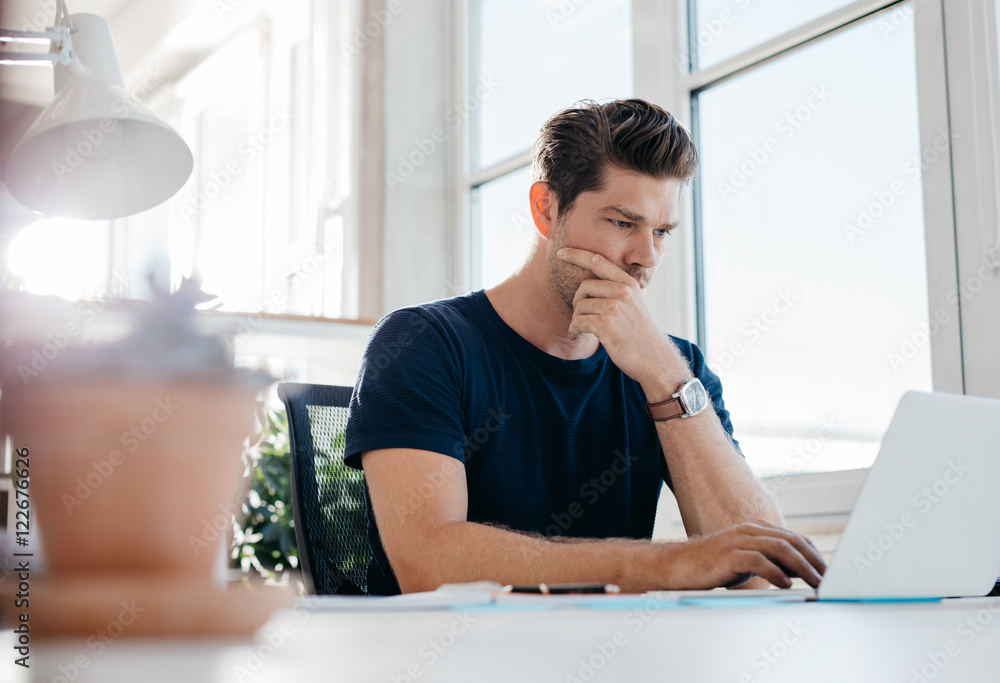 Pensive young male executive using laptop at his desk