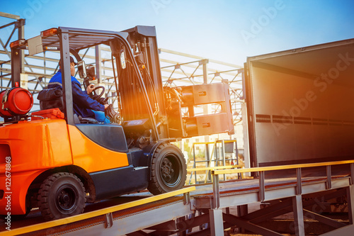 Foto Forklift is putting cargo from warehouse to truck outdoors