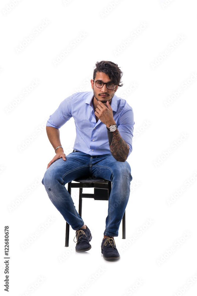 Portrait of brunette young man in light blue shirt and jeans, sitting on  chair in studio shot isolated against white background. Full length photo  Stock Photo | Adobe Stock