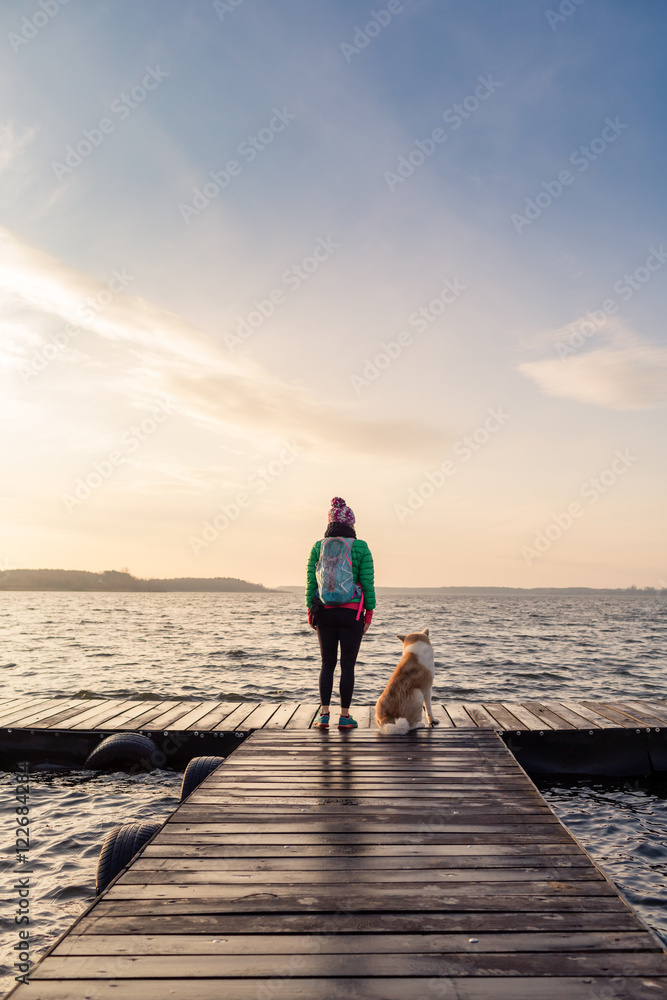 Naklejka premium Woman with dog enjoy sunrise at lake, backpacker looking at beautiful morning view