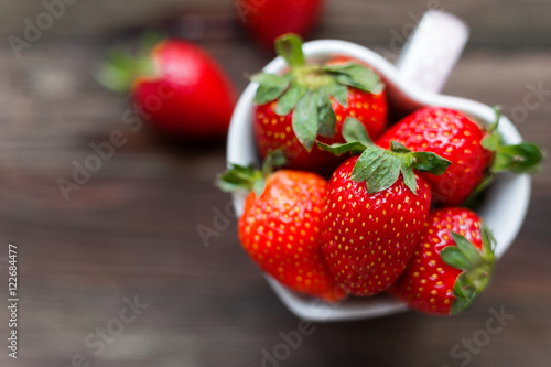 Fresh juicy strawberries in cup shaped as a heart  symbol of love. Rustic wooden background. Top view  place for text.