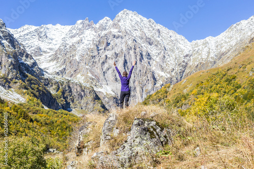 Young woman standing on stone and looking at snowy peak