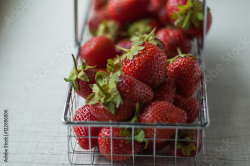 Strawberries in a small metal basket on a table.