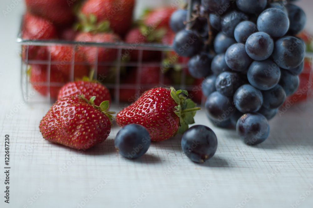 Strawberries and grapes in a small basket on a metal table. Strawberries and grapes in a small basket on a metal table.