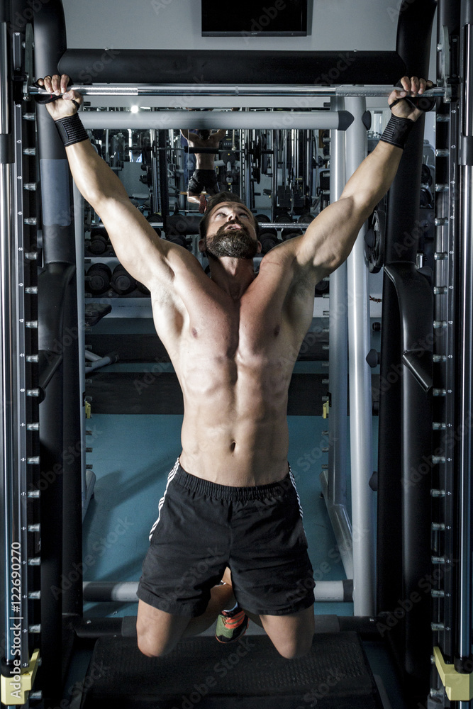 Fotografia do Stock: Entrenando en el gimnasio. Hombre con grandes músculos  levantando peso mientras entrena en el gimnasio. Ponerse en forma.