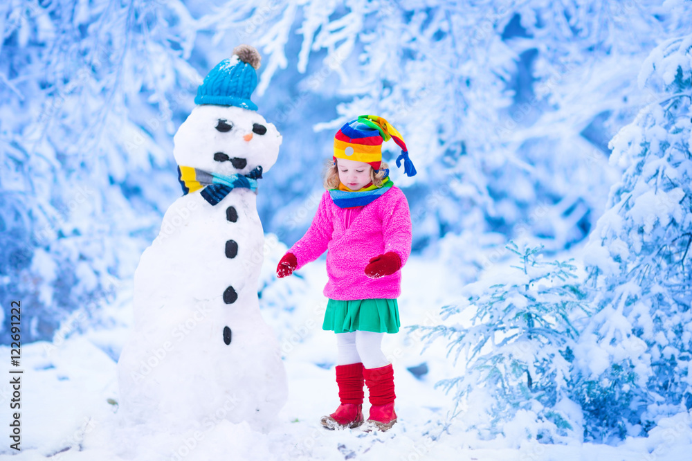 Little girl building a snow man in winter
