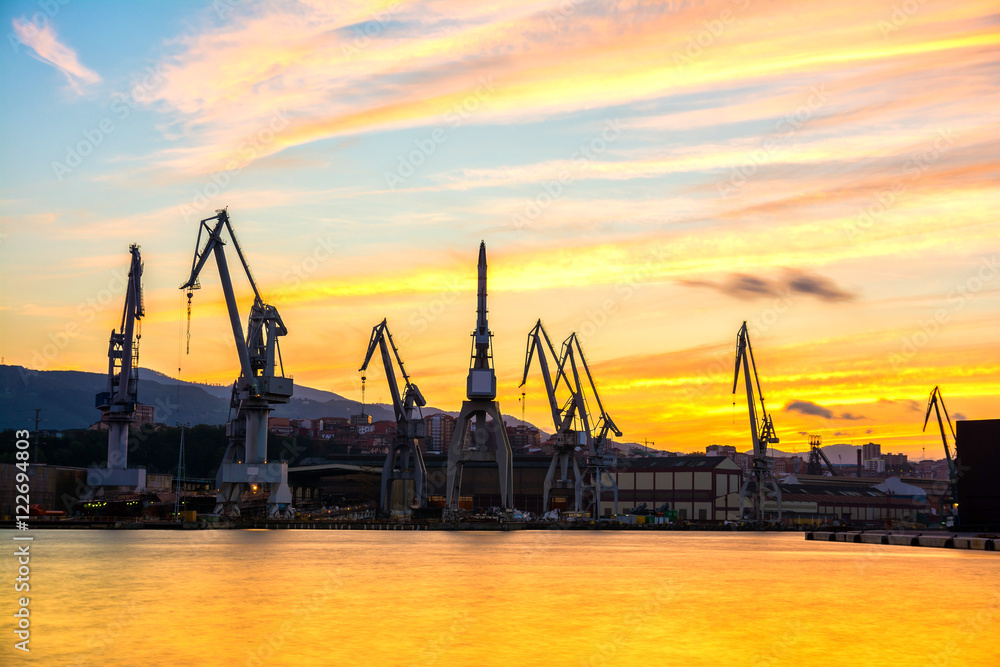silhouetted cranes at dusk at shipyard
