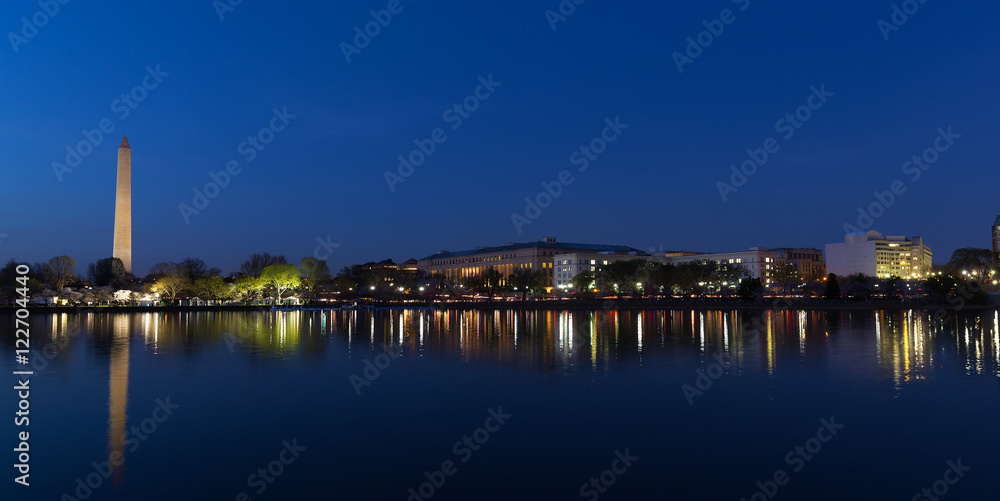 Night panorama of Washington DC during cherry blossom festival. Washington Monument and lights reflection in Tidal Basin waters.