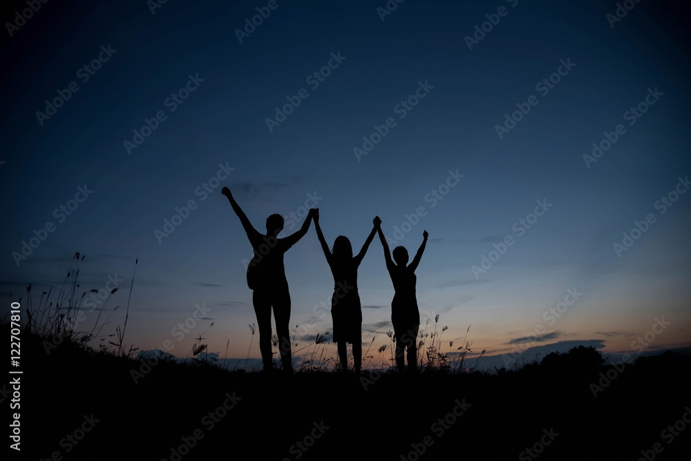 Friends holding hands up at sunset.