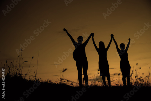 Friends holding hands up at sunset.