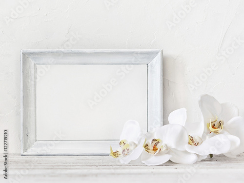 White photo frame with white orchids on the vintage table. Frame