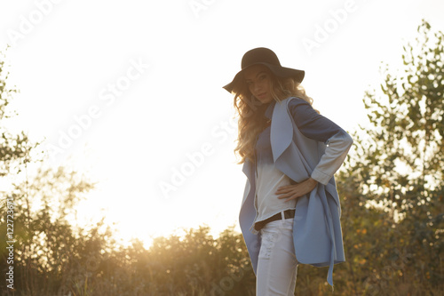 Stylish woman in hat at nature, sunset background