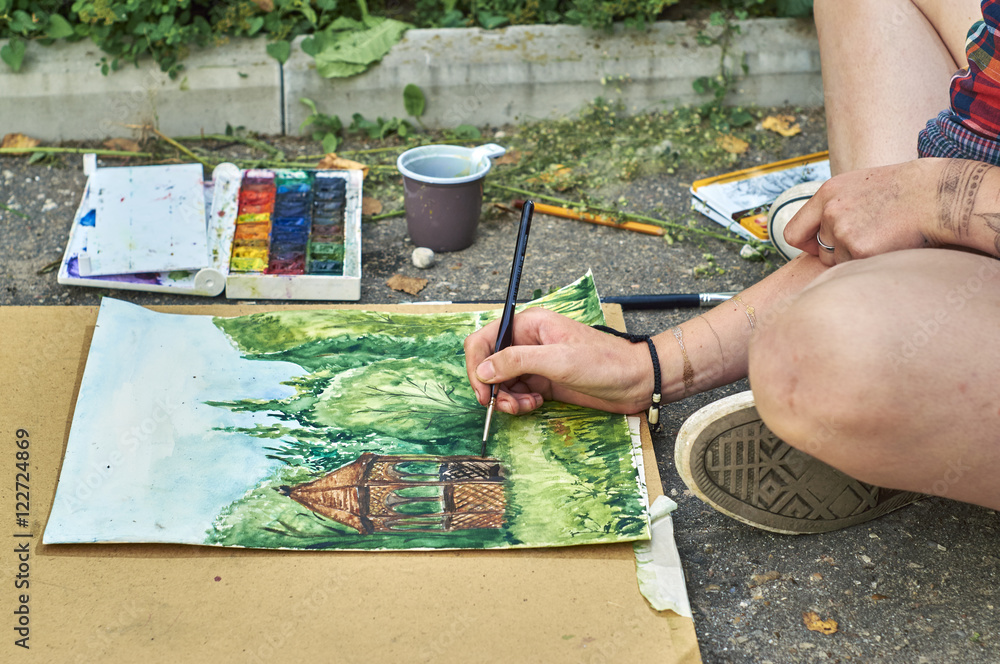 Naklejka premium Young girl is painting a watercolor picture sitting on the pavement 