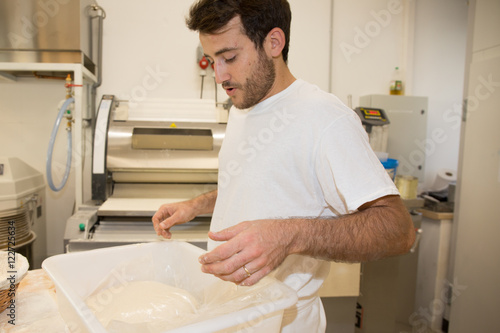 Cheerful baker man making dough at bakery