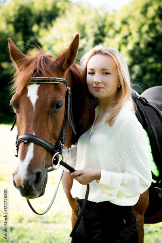 Молодая девушка со светлыми волосами стоит рядом с коричневой лошадью  © natasidorova 
