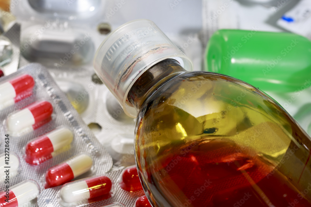 Close-up of syrup bottle and bundles of capsules and pills. Expired medications Close-up of syrup bottle and bundles of capsules and pills. Expired medications