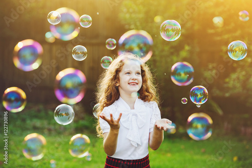 Beautiful child enjoying blowing soap bubbles in the summer on n