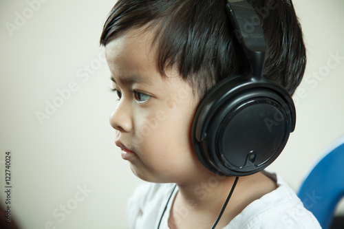 Happy cheerful boy with headphones listening to music on a gray